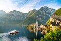 Panorama view of famous old town Hallstatt and alpine deep blue lake with tourist ship in scenic golden morning light on a beautif