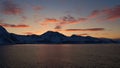 Panorama view after sunset of snow-covered mountains at the Norwegian coast with orange colored clouds reflected in the water. Royalty Free Stock Photo