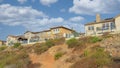 Panorama White puffy clouds Dirt uphill trail on a rocky slope outside the fenced homes at S