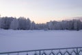 A panorama of the winter park. Frozen river, snow-covered trees, power lines and poles. Sunset, polar night. Royalty Free Stock Photo