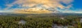 Panoramic aerial view over a wide forest with the undergoing sun, covered by enlightend clouds Royalty Free Stock Photo