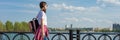 Panoramic banner of female student going outdoor. Teen girl in white t-shirt with backpack, background sky with clouds Royalty Free Stock Photo