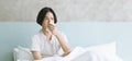 Panoramic banner image of sick Asian man sitting on bed holding tissue handkerchief blowing running nose feels unwell unhealthy. Royalty Free Stock Photo