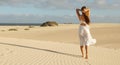 Panoramic banner view of beautiful woman with white dress walking on desert dunes at sunset. Girl walking on golden sand on Royalty Free Stock Photo