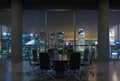 Panoramic conference room in modern office, cityscape of Singapore skyscrapers at night. Black chairs and a black round table.