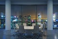Panoramic conference room in modern office, cityscape of Singapore skyscrapers at night. White chairs and a white round table.