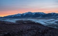Panoramic mountain landscape with long snowy mountain range lit by dawn sun among low clouds. Awesome alpine scenery with high
