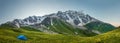 Panoramic mountains landscape with tent in tourist camp on grassy mountain valley. Hiking in mountains. Trekking in wild nature Royalty Free Stock Photo