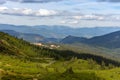 Panoramic mountains view with village and shadow of clouds on green forest valley. Carpathian mountains in perspective.