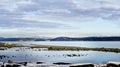 Panoramic ocean view of distant snow covered mountains on a bright, slightly cloudy day. Royalty Free Stock Photo
