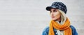 Panoramic outdoor profile portrait of beautiful young blonde girl with blue eyes wearing orange scarf, denim jacket and plaid cap. Royalty Free Stock Photo