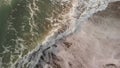 Panoramic overfly on rough ocean waves crashing shore with lot of white foam and emerald-colored water and dark sand