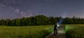 Panoramic photo of a man with his bike watching the beauty of the milkyway at the dark night sky at the countryside.