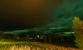Panoramic photo of strong bright Aurora Borealis behind heavy clouds, meadow and birch trees look very dramatic. Joesjo, Lapland,