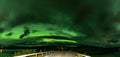 Panoramic photo of strong bright Aurora Borealis behind heavy clouds over road, Joesjo Lake and Scandinavian mountains in Swedish