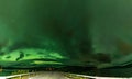 Panoramic photo of strong bright Aurora Borealis behind heavy clouds over road, Joesjo Lake and Scandinavian mountains in Swedish