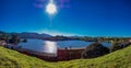 Panoramic photo of water reservoir in the city of Pocos de Caldas with blue sky and sun shining in the sky with lens flare