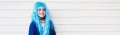 Panoramic portrait of happy teenage girl with blue hair, on background of white wall with lines.
