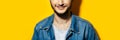 Panoramic portrait of young smiling guy wearing denim jacket on studio background of yellow color. Royalty Free Stock Photo