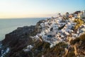 Panoramic scene in sunset light of Oia windmill and white building townscape along island natural mountain facing vast ocean