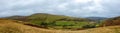 A panoramic scenic view of a mountain valley with grassy green slope, green fields and trees under a stormy grey sky Royalty Free Stock Photo