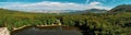 Panoramic shot of a beautiful landscape with hills, a forest and a small lake on a sunny day Royalty Free Stock Photo