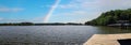 A panoramic shot of the blue waters of Lake Acworth with a white wooden fence surrounded by lush green trees, grass and plants Royalty Free Stock Photo