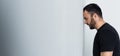 Shot of depressed bearded man standing by white wall with closed eyes