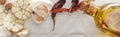 Panoramic shot of garlic cloves, dried chili peppers and bottle with oil on white paper background.