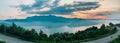 Panoramic shot of a road surrounded by greens under the cloudy sky