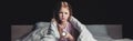 Shot of scared child sitting on bedding and holding flashlight isolated on black