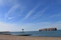 Panoramic shot of a shore, a huge transport ship with containers boating in the sea and the blue sky