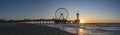 A panoramic shot of the sun setting beside the Pier in Scheveningen with the ferris wheel and the bungy jump tower Royalty Free Stock Photo