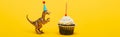 Panoramic shot of toy dinosaur in party cap and cupcake with candle