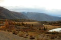 Panoramic shot of a winding road along a river bed skirting mountain ranges in early autumn