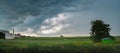 Alone tree in a field and a garage under a sky with clouds before a storm on a summer outside the city in the Royalty Free Stock Photo