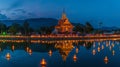 A panoramic view of a Buddhist temple lit by thousands of candles during Visakha Bucha Day at dusk, reflections on a Royalty Free Stock Photo