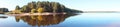 Panoramic view of the forest island, pond or lake. The reflection in the water. Beautiful widescreen autumn landscape.