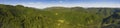 Panoramic view of forested hills and a glade on a bright day.