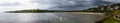 A panoramic view of the Inchydoney beach on an overcast day with people surfing, swimming, and enjoying the warm weather