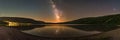 A panoramic view of a lake reflecting the milky way and starry sky at night with hills on either side Royalty Free Stock Photo
