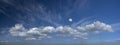 A panoramic view of large cloud formation with waxing moon.