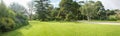 Panoramic view of a large formal garden landscaping with well-tended neat lawn and a variety of trees, flower beds and walkway.