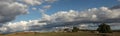 Panoramic view of large open dry drought affected farm fields under stretching cloud filled blue skies with farm buildings in