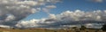 Panoramic view of large open dry drought affected farm fields under stretching cloud filled blue skies with farm buildings in