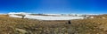 Panoramic view of a man sitting alone at the Deosai plains national park, land covered by snow.