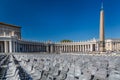 Panoramic view of many empty grey chairs on St. Peters Square with people and Vatican building.