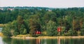 Panoramic View On Many Red Swedish Wooden Sauna Logs Cabins Houses On Island Coast In Summer Cloudy Day. Swedish Old Royalty Free Stock Photo