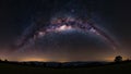 Panoramic view of the Milky Way galaxy arching over a dark landscape with rolling hills and a lone tree Royalty Free Stock Photo