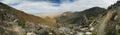 A panoramic view of a mountain range with a few trees and a rocky hillside